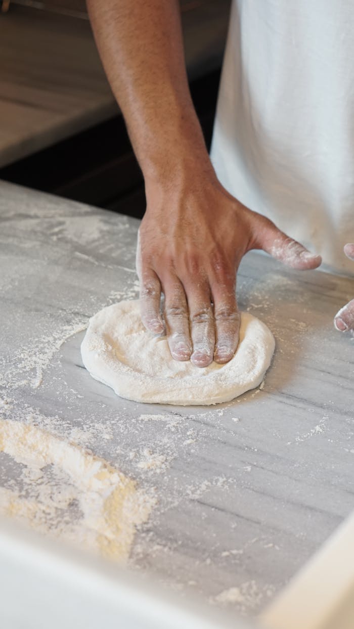 Close-up of a chef's hands preparing dough for homemade pizza on a floured surface.